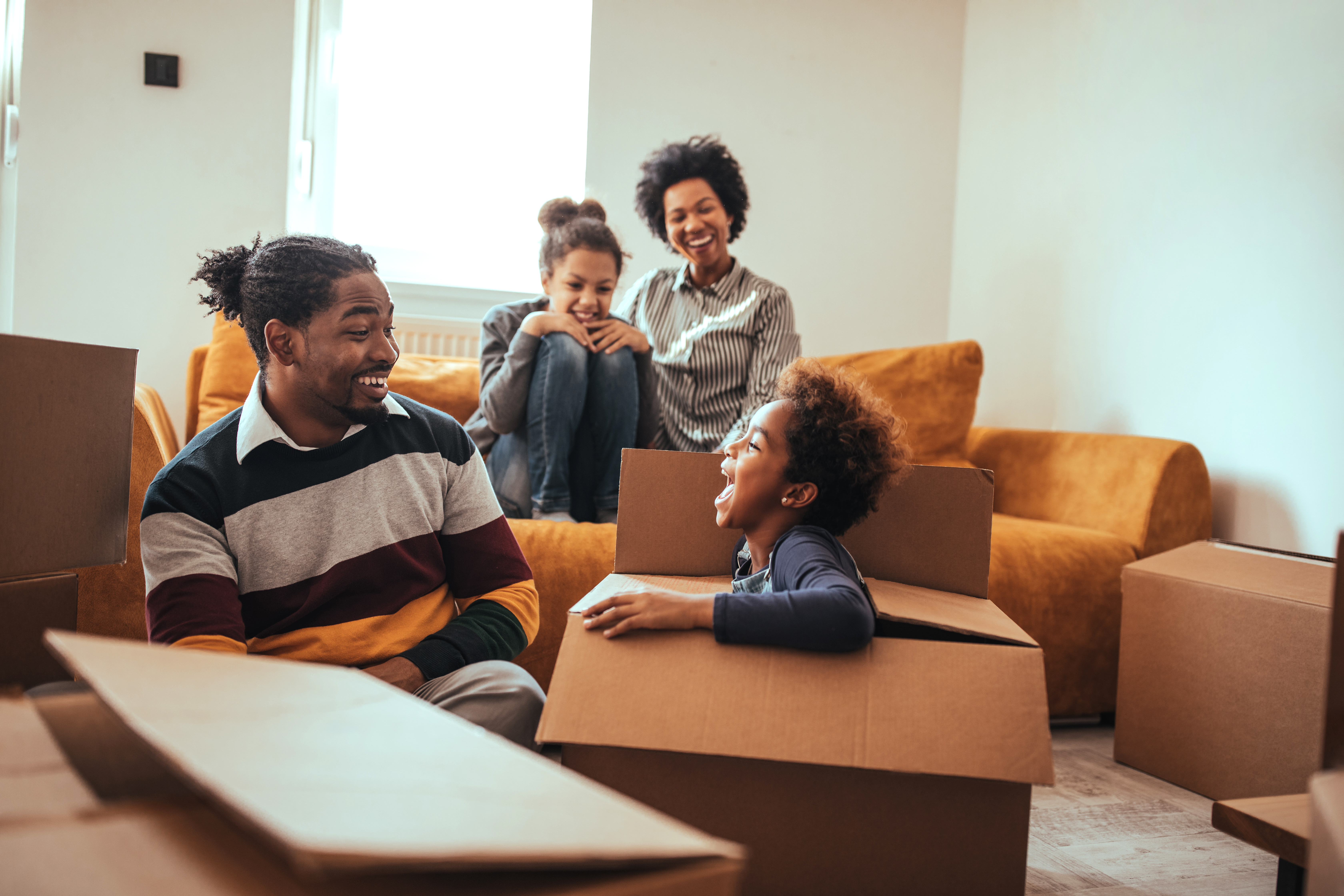 A family enjoys a game of hide and seek while unpacking boxes in their new home.